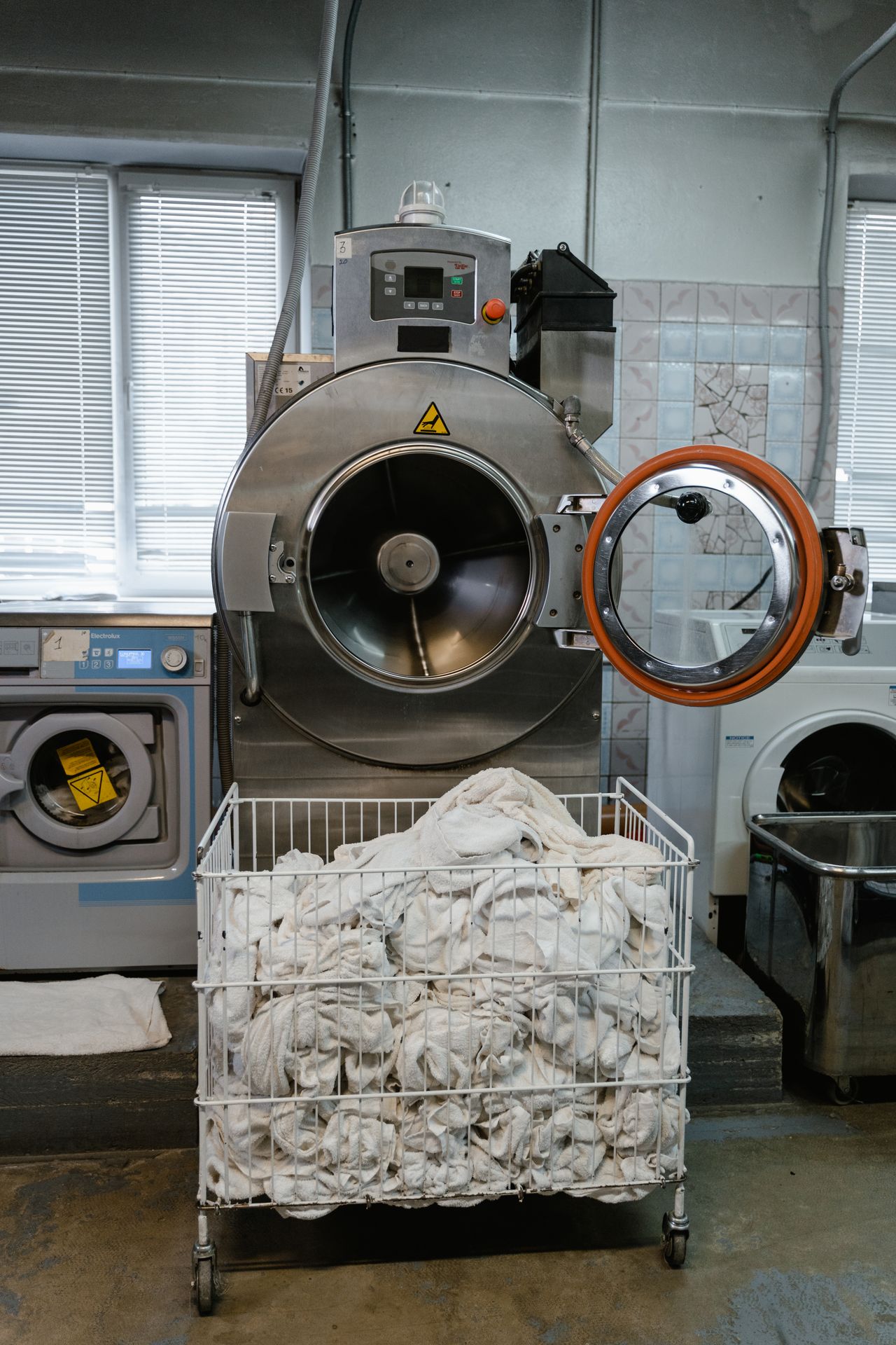 Lavatrice industriale aperta e un carrello di biancheria appena lavata